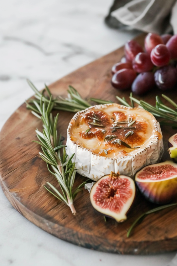 Baked brie surrounded by colorful fruits, rosemary sprigs, and berries for added visual appeal