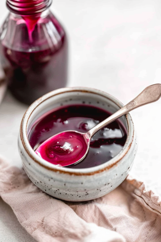 Close-up of a small bowl of pink jam with a spoon and a bottle of food coloring nearby